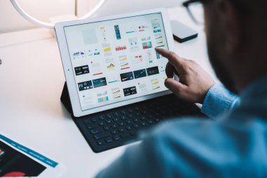 Ofisteki beyaz bilgisayar masasında oturan ve grafik şemasını seçerken tableti tıklatan bir adamın arka plan görüntüsü 