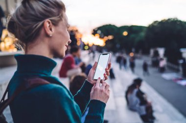 Web sitesi için 4G kablosuz bağlantıya bağlı yeni bir ülkeyi keşfetmek için boş akıllı telefonlu video rehberi izleyen binlerce yıllık kadının arka planı, kopyalama alanı ile cep telefonunu taklit edin