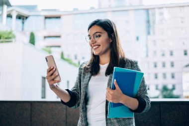 Neşeli milenyum kadın blogcusu akıllı telefon uygulamaları ve caddede duran kamera kullanarak video bloğu için konuşuyor, olumlu hippi kız 4G internet ve cep telefonuyla video görüşmesi yapıyor.  