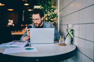 Günlük kıyafetli bir erkek, cep telefonu operatöründen mesaj alıyor. Kafede bilgisayar ve kağıtlarla çalışırken haberlerle hayal kırıklığına uğruyor. 