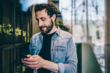 Kendine güvenen, rahat giyinen, telefonla konuşan sosyal medyada sohbet eden, modern kafede zaman geçiren bir adamın camından bakın.