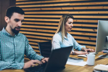 Geliri analiz eden bilgisayar kullanan genç bir adamla ofis masasında oturan sıradan giyinen bir kadın proje üzerinde çalışıyor.