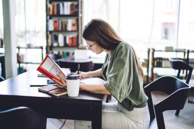 Lang saçlı, çalışkan, kitap yazmaya ve açık kütüphanede kitap tutmaya odaklanmış bir kadının yan görünüşü