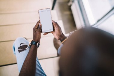 Yukarıdan gelen siyah kel adam eğleniyor ve merdivenlerde otururken boş ekranlı cep telefonu kullanıyor.
