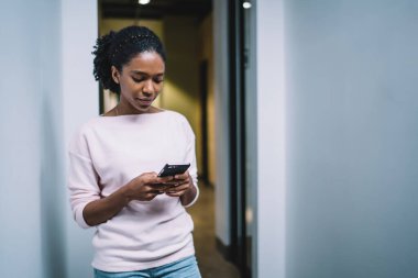 Modern Afro-Amerikalı kadın ofis binasının koridorunda dururken cep telefonu ve mesaj kullanıyor.