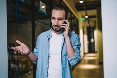 Günlük gömlekli genç adam ofis koridorunda akıllı telefonla konuşuyor ve olaya müdahale eden kişiye bakış açısını açıklarken el kol hareketi yapıyor. 