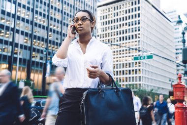 Kentin modern işlek sokaklarında yürürken gözlüklü, kendinden emin, başarılı Afrikalı Amerikalı kadın çalışan cep telefonuyla konuşuyor.