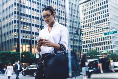 Modern şehrin sokaklarında dikilirken cep telefonuyla mesajlaşan gözlüklü, şık, Afro-Amerikan kadın işçilere odaklanmış.