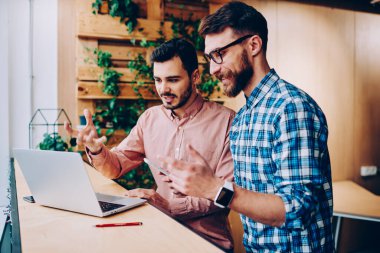 Zeki erkek iş ortakları şık günlük gömleklerle iş projelerini tartışırken birlikte dizüstü bilgisayar kullanıyorlar ve modern kafede gülümsüyorlar. 