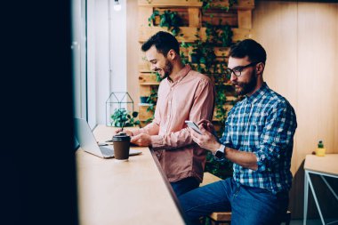 Gündelik kıyafet giyen heyecanlı erkek, modaya uygun bir adamın kafede dizüstü bilgisayar kullanarak akıllı telefonlara baktığı, kahve içtiği bir proje yaratıyor.