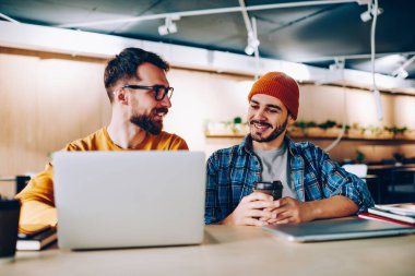 Gündelik kıyafetlerle tatmin olmuş erkek. Laptop kullanıyor. Şapkalı, kafede kahve içen modaya uygun bir adamla proje yapıyor.
