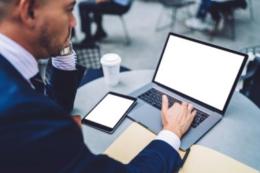 Ekin işadamının klavyede daktilo yazarken ve tablet kullanırken sokak kafesinin masasında oturup tek kullanımlık bardakta içki içerken yan görünümü