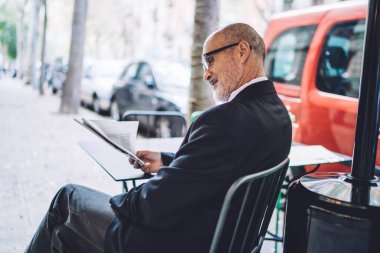 Takım elbiseli ve gözlüklü yaşlı kel bir adamın arka planda oturup bulanık şehir geçmişi hakkında gazete okuması. 