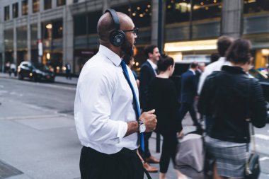 Afrika kökenli Amerikalı kel sakallı ofis çalışanı kalabalık caddeyi geçerken kulaklıkla müzik dinliyor.