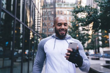 Keyifli kel Afrikalı Amerikalı sporcu sosyal medyada video seyrediyor. Mola sırasında şehirde yürürken kulaklık kullanıyor.