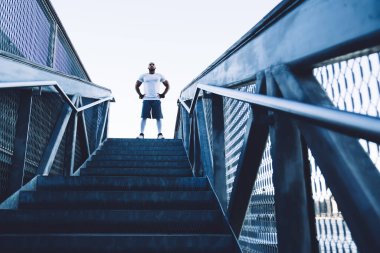 Aşağıdan tanınmayan Afro-Amerikan spor giyim eğitmeni ve merdivenlerin başında durup kameraya bakan eldivenler.
