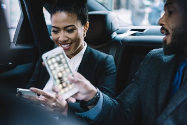 Neşeli zarif bir bayan cep telefonu kullanıyor iş arkadaşıyla gülüyor resmi takım elbiseli Afrikalı Amerikalı bir erkekle konuşuyor arabada arka koltukta oturuyor.