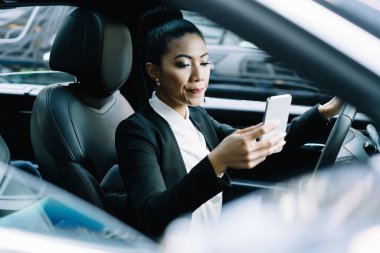 Sakin, zarif elbiseli, araba süren, sakin, etnik bir bayan. Modern arabaları sürüyor, sosyal medya mesajları yazıyor. Cep telefonunda direksiyon başında oturuyor.