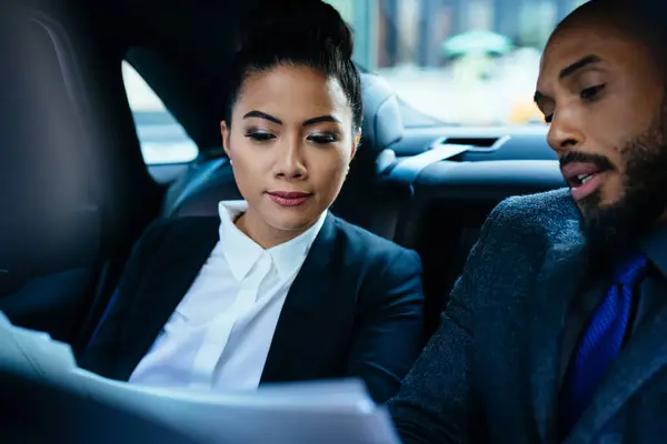 Confident elegant lady looking at documents reading contract negotiating with executive man discussing strategy of company sitting on back seat in car