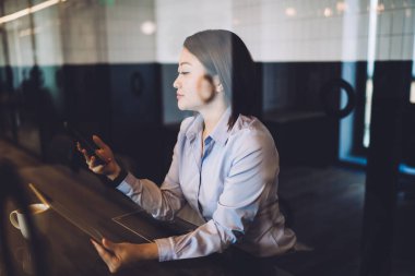 Klasik giyinmiş yetişkin, güzel bir kadın. Akıllı telefonlarda uygulama kullanıyor ve kafede elinde kahve tableti tutuyor. 