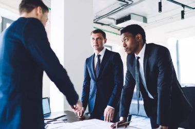 Ofis ortamında dokümanları olan çeşitli başarılı ortaklarla konuşurken dikkatli bir şekilde odaklanmış zeki erkek çalışan.