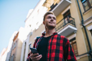 Kayıp gezginlerden kırmızı-siyah tişörtlü gezginler şehirde yazın binanın karşısında duran cep telefonlarını izliyorlar. 