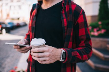 Günlük kıyafetleri olan, sosyal medyada gezinen, cep telefonunu iletişim için kullanan sıcak içeceklerle gezen bir adamın görüntüsü.