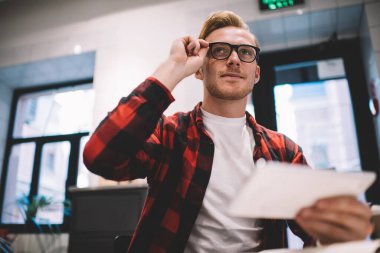 Kendine güveni tam, genç, serbest çalışan, gözlük takan iş yerinde akıllı telefonu kullanarak yüzünü çeviren biri.