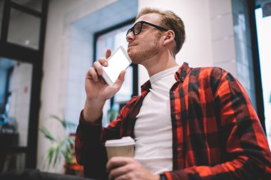 Düşünceli, kafası karışmış, kafası karışmış bir erkek cep telefonuyla yan gelip yatarken ve boş ekranla başka tarafa bakarken projeyi düşünüyor.