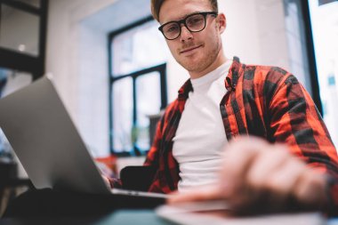 Ekin gülen, kareli tişörtlü, iş yerinde dizüstü bilgisayarda serbest iş sırasında masada uzanan akıllı telefonu kontrol eden genç adamdan.