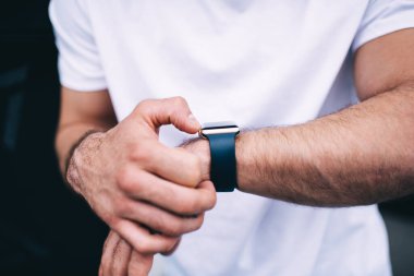 Tüylü beyaz gömlekli sıradan bir erkek, modern stil akıllı saati dokunmatik ekranla kontrol ediyor. 