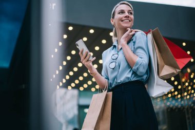 Elinde alışveriş çantaları ve akıllı telefonlar tutan neşeli beyaz kadın Kara Cuma boyunca gözlerini kaçırıyor. Çekici, gülen bir kadın alışveriş merkezinde boş vakitlerin tadını çıkarıyor.