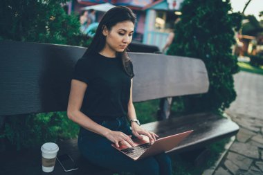 Ciddi Asyalı kadın serbest yazar, dizüstü bilgisayarda sosyal ağ daktilo yayını, düşünceli hipster kız blogları ve eşit derecede bankta oturan multimedya paylaşımı üzerine yoğunlaştı.