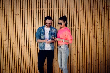 Sokak kıyafetleri giyen hippi bağımlıları promosyon amaçlı ahşap fon ile reklam alanında duran sosyal ağlardan PDA takipçileriyle mesajlaşmak için modern cep telefonu cihazları kullanıyorlar.