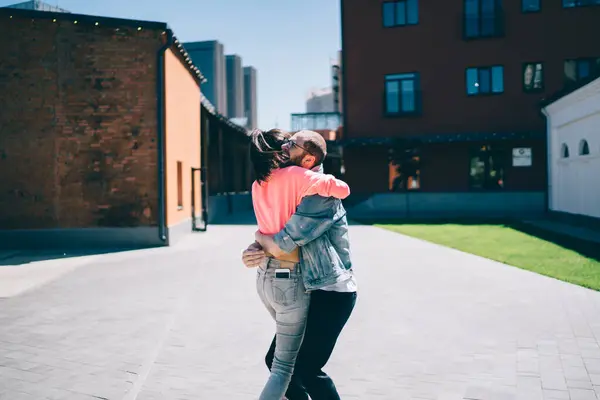 Caucasian emotional couple in love dressed in stylish cool clothing having fun during sunny date at urban setting in city, joyful sincerely male and female hug during mood positive feelings