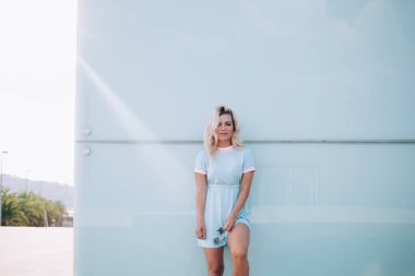 Güneşli bir günde şehirde vakit geçirirken modern binaların duvarına yaslanmış güneş gözlüklü moda bir kadın.