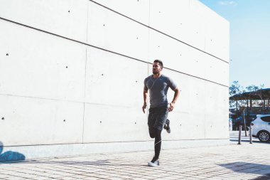 Spor elbiseli, kulaklıklı, müzik dinleyen, şehir sokağında güneş altında egzersiz yapan aktif bir erkekten.