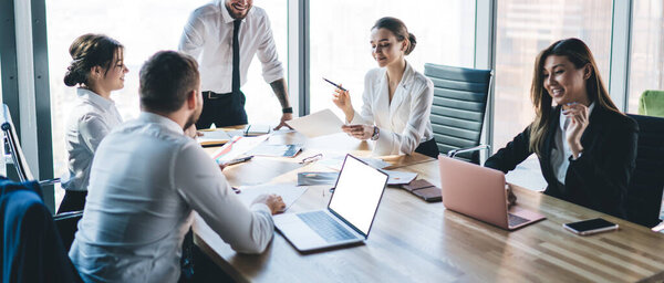 Руководитель группы по сбору урожая, стоящий и говорящий о процессе работы, в то время как коллеги сидят за столом и делают заметки в офисе 