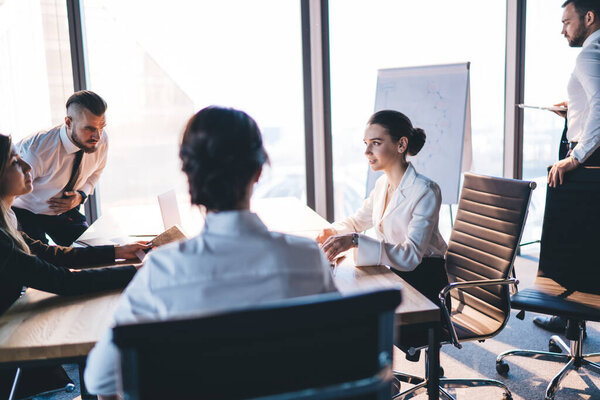 Вид сбоку на занятый персонал, читающий отчет за деревянным столом, сидя за удобным офисным креслом в легком бизнес-центре с современным интерьером