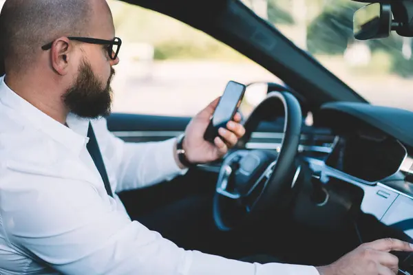 stock image Businessman reading received smartphone notification while using self-driving in contemporary car with autopilot, male tracking gps location via cellphone application connected to 4g wireless