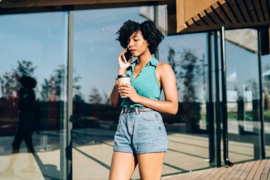 Kıvırcık saçlı güzel Afro-Amerikalı kadın, güneşli yaz günlerinde açık havada dolaşırken bankacıya sesleniyor. Akıllı telefonuyla konuşan çekici bir kadın, elinde kahve bardağını doldurmak için kahve tutuyor.