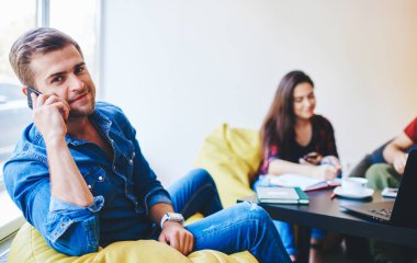 Meslektaşı arka plandaki işten bahsederken yakışıklı, neşeli, bin yıllık erkek portresi teslimat servisine telefon eden öğrenci lideri.