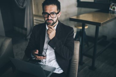 Şık takım elbiseli, dizüstü bilgisayarlı ve bacaklı kafası karışık bir adam. Akıllı telefon kullanıyor. Ortağıyla iletişim kuruyor.