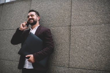 Elinde büyük bir klasörle gülümseyen ve cep telefonuyla konuşan başarılı adamdan şehrin beton duvarına yaslanmış, başka yöne bakan.