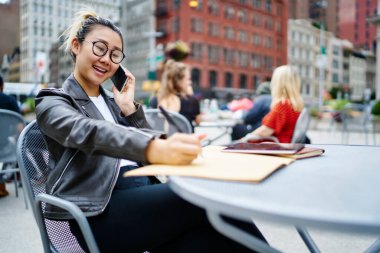 Mutlu Çinli kadın ders kitabına not alıyor. Arkadaşça cep telefonu sohbetleri sırasında son moda gözlüklü neşeli hippi kız kaldırım kafesinde oturup uluslararası konuşma çağrısında bulunuyor.