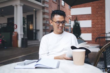 Genç Asyalı hevesli, zeki, pozitif öğrencinin üniversitede eğitime hazırlanırken dışarıda kafede oturup ders kitabı okuması sırasında tatmin olmuş.