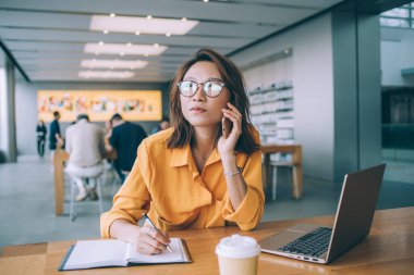 Klasik gözlüklü, düşünceli bir kadın. Uzaktan kumanda sırasında cep telefonuyla gelen haberleri dinliyor. Müşteri hizmetleriyle iletişim kuran Asyalı kadın hakkında kafa yoruyor.