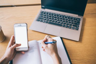 Modern akıllı telefon kullanan ve Hong Kong şehrinde defter ve kahve fincanı olan ahşap masaya notlar yazan ince kadın elleri.