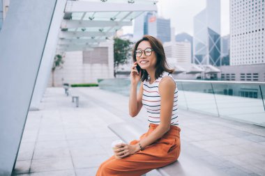 Hong Kong 'da telefonla konuşurken elinde plastik bardakla oturmuş bankta gülümseyen Asyalı güzel bir genç kadın.