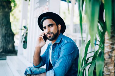 Şık şapkalı, kotlu tişörtlü, sakin İspanyol bir adam. Kafenin merdivenlerinde dinlenirken cep telefonundan arıyor.